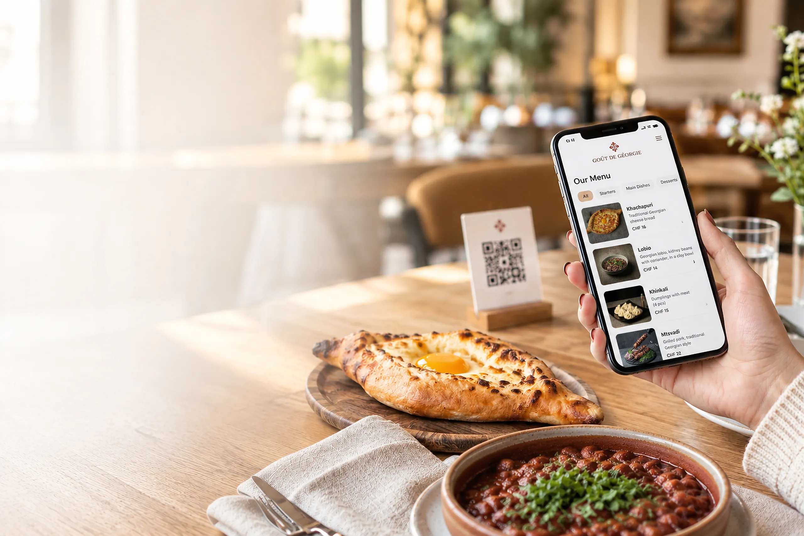 Guest browsing the Goût de Géorgie QR menu on a phone, with khachapuri, lobio and a QR code stand on the table