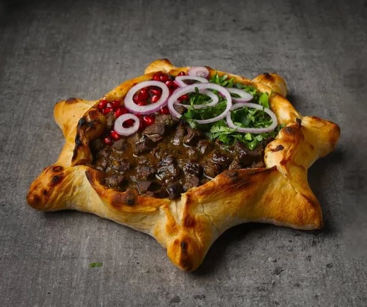 Bread boat filled with braised beef, red onion, herbs and pomegranate