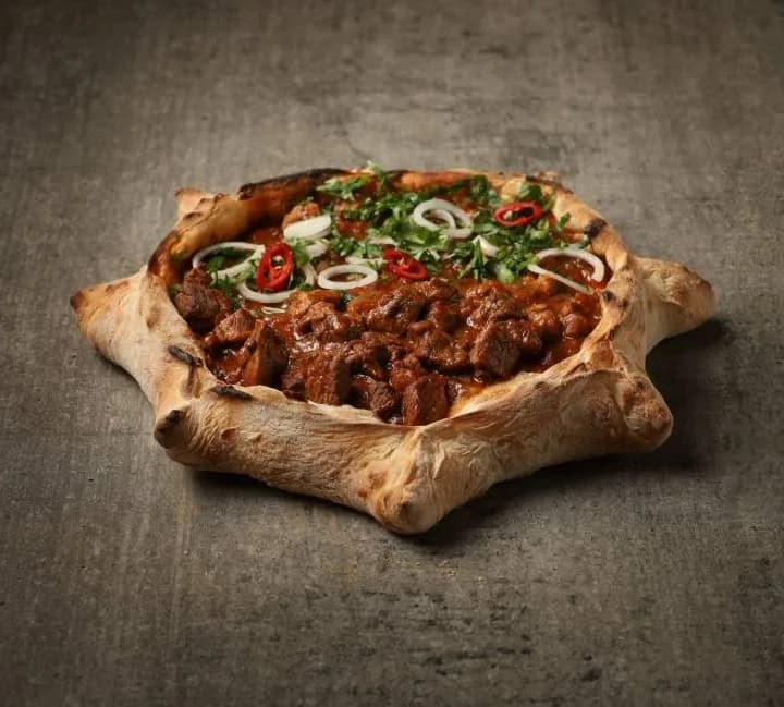 Bread boat filled with beef stew, onion, chili and fresh herbs