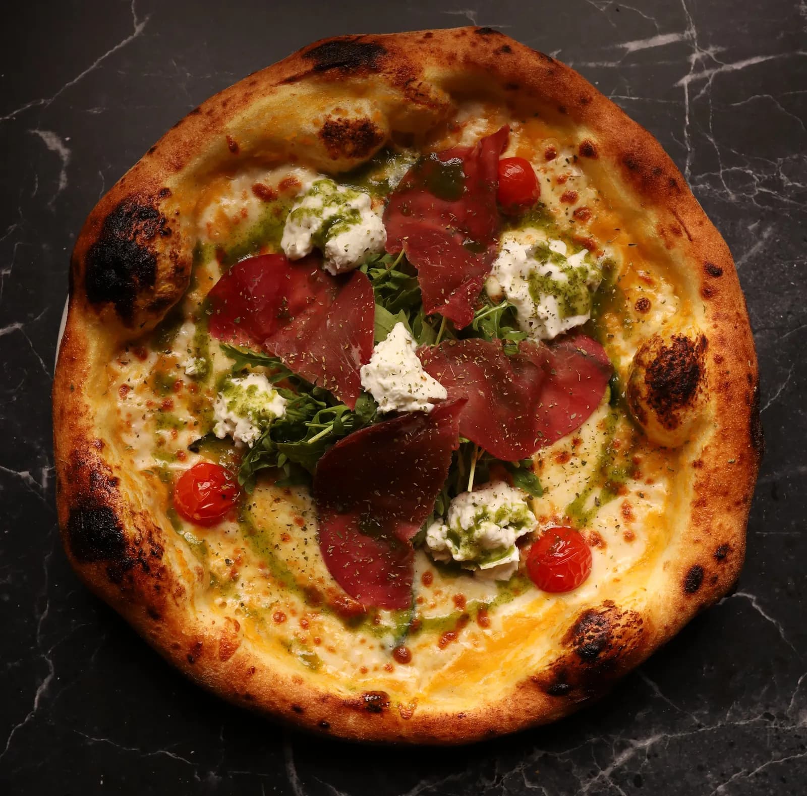Wood-fired pizza with bresaola, burrata, rocket, cherry tomatoes and pesto