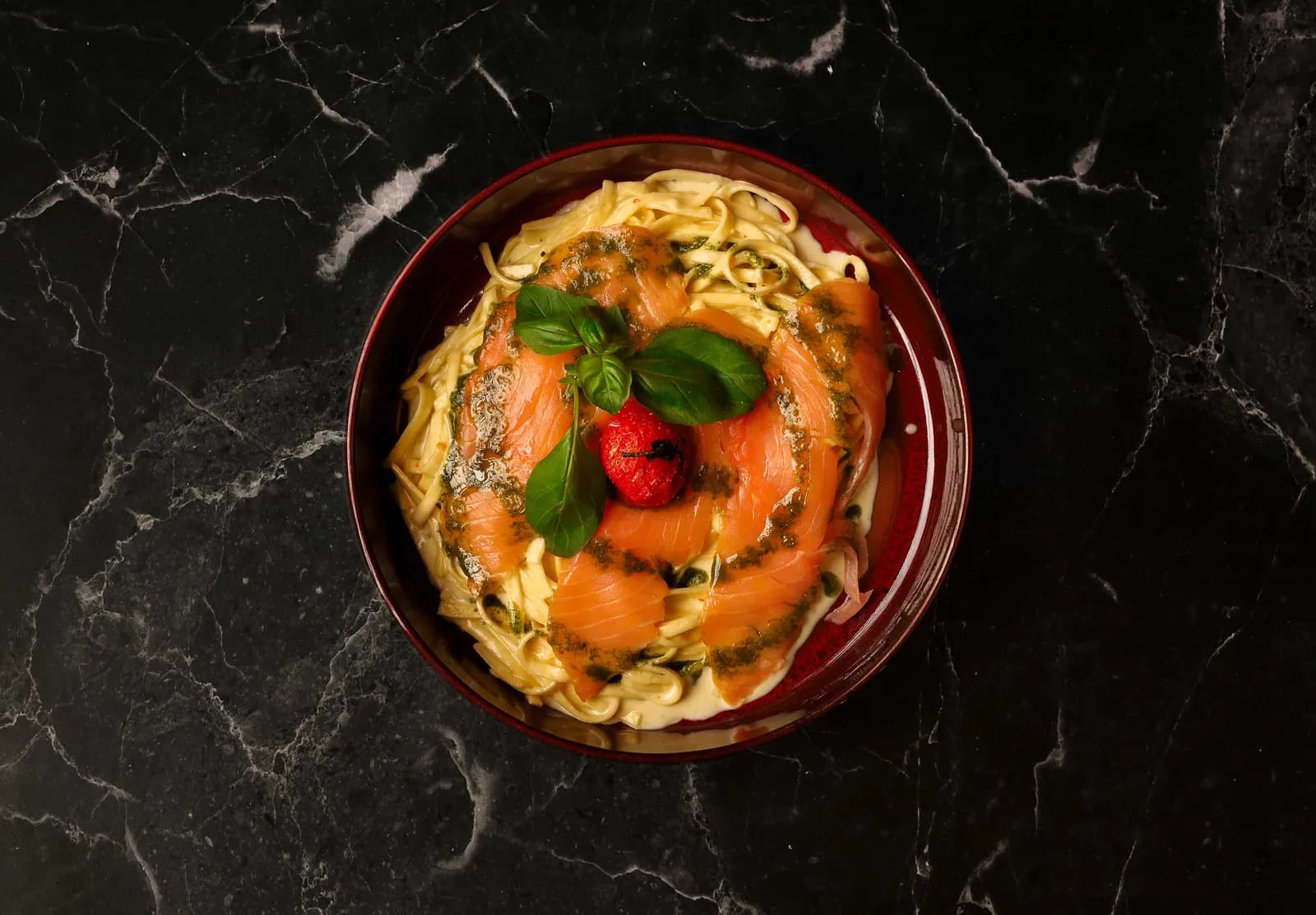 Tagliatelle with smoked salmon, basil pesto and roasted cherry tomato on dark marble