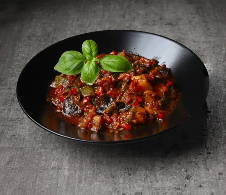 Slow-cooked vegetable stew with basil in a black bowl